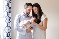 Husband and wife holding and looking down at their newborn baby in their arms