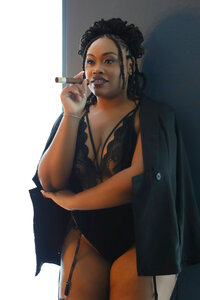 A beautiful woman poses in a black bodysuit and a black jacket wile holding a cigar during her Las Vegas boudoir session.