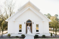 Bridal portrait of bride in white lace dress and cathedral veil standing in front of chapel at Four Fifteen Estates wedding and elopement venue in New Boston, Texas