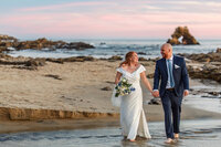 A bride and groom walking on a SoCal beach on their wedding day.