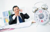 Image of a man sitting at a desk with  a clock in the forground signifying time saved