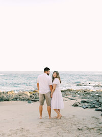 beach photo of bride looking back at the camera while groom looks at the ocean