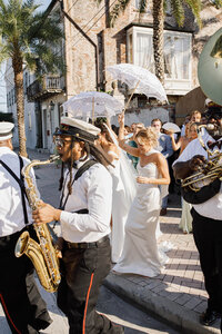 A photo of a bridal party walking with a band walking the streets of New Orleans 