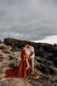Couple and baby cuddle on beach cliff