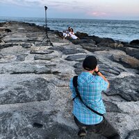 Photographer photographing Couple sitting on rocks at New Jersey Shore engagement session