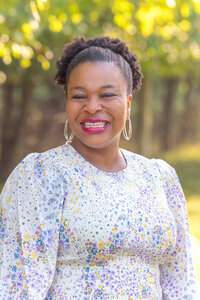 A woman smiling and posing for her headshot at a park.