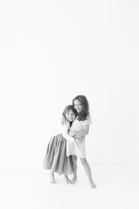 A black and white image of two little girls hugging and looking at the camera during their in-studio photography session.