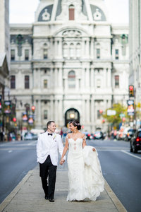 Couple walking hand in hand down Broad Street in Philadelphia, with the city skyline in the background.