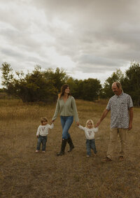 A toddler boy walking with his dog in a grass field.