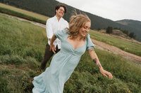 Man and woman holding hands while laughing and running through a field