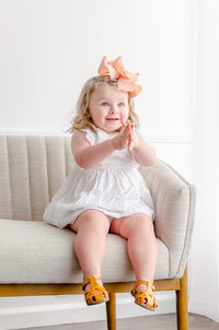 a little girl claps her hands on a couch in the studio