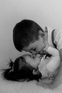 Schwarz weiß Bild von einem Bruder und einer Schwester, wie der Bruder der kleineren Schwester einen Kuss gibt