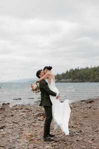 A person holding up their partner as they kiss on the water's edge 