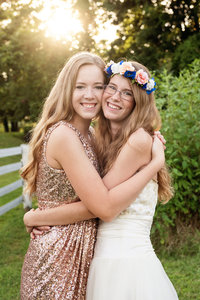 Sorority sisters smiling at camera hugging on another as golden hour. One is wearing a flower crown