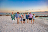 Extended family walking hand in hand along the water on the beach with the sunset behind them.
