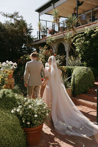 La Playa Carmel Wedding Day. Couple in wedding attire holding hands and walking through venue garden