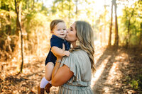 Mom kisses her little boy during a family session in  the woods located near Birmingham