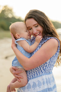 mom and baby in blue and white snuggling on the beach at golden hour