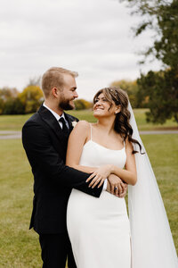 A newlywed couple with their arms around each other as one looks back at the other