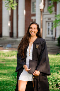 Classic portrait of college senior standing on Vanderbilt campus wearing a white dress and cap and gown
