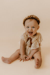 Photo of Morgan's 7 month old daughter in a dress and flower crown smiling at the camera in the studio.