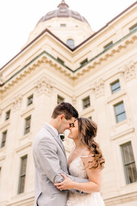 Bride and groom with their arms embracing each other as they face one another with foreheads touching in front of the Kansas Capitol during wedding portraits by Kansas City Wedding Photographer Sarah Riner Photography