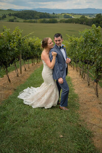 The bride is hugging the groom from behind at their wedding at a vineyard.