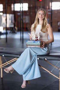 Professional brand photography of a client in a blue and white outfit, seated in a journalist-style chair with books. Capturing her personality and profession through intentional brand visuals