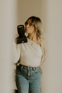 Laura, photographe du duo the soulmate duo, assise dans un décor cosy, grimace en tenant un appareil photo.