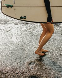 Woman holding horizontal surfboard walking along the beach