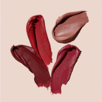 Artistic flat lay of lipstick swatches in various red and nude tones on a soft pink background, styled by Ylva Erevall.