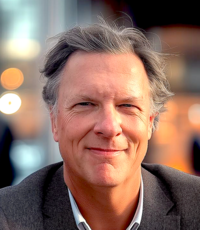 man with gray hair looking at the camera with a closed lip smile