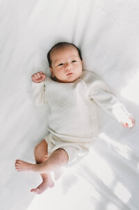 newborn baby in a cozy knit outfit on a white bed