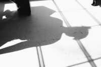 black and white shadow of woman sitting on bench and lines from industrial windows on white floor at studiostudio in ann arbor michigan