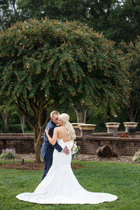 Bride and groom snuggling outside showing off back of bride's dress at First Wesleyan Church by Charlotte wedding photographers DeLong Photography