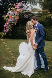 Bride and groom kiss under the wedding arch on a gras-field.