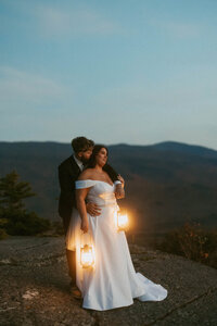 Bride and groom holding lanterns, looking at the sunset in the White Mountains of New Hampshire.