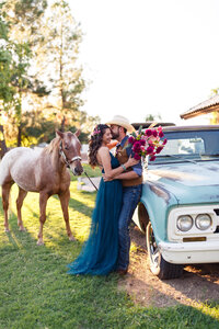 country western couple kissing near an old turquoise truck with their horse