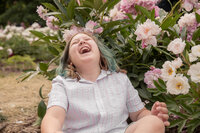 boy throws his head back in laughter while sitting next to blooming peony bush at nichols arboretum in ann arbor michigan