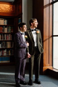 grooms holding hands looking out the window