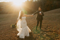Bride holding flowers and holding hands with a groom at sunset at The Preserve at Chocorua in New Hampshire.