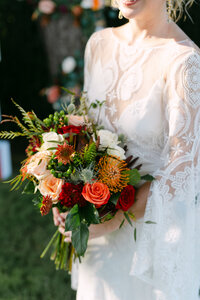 A bride stands in a sunlit field, gracefully holding her bouquet, surrounded by nature's beauty and tranquility.