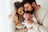 Newborn baby girl being kissed by parents on newborn photoshoot