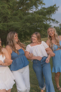 Four senior girls have their arms interlocked looking at each other and laughing. They are in a grassy field with trees behind them at Willow Springs Park in Johnson City, TN. 