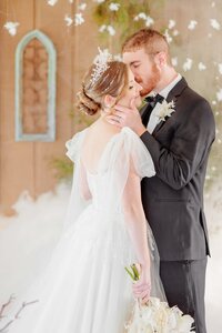 The groom kisses his bride on the cheek and cradles her face.