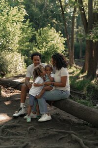 Black family sitting on a log and snuggling in front of the White River during outdoor family photography session at Holiday Park in Indiana.