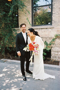 Wedding photo of female, Aislynn Palmer Wedding photographer, with her newlywed Husband wearing a bridal dress and holding flowers; turning towards each other laughing.