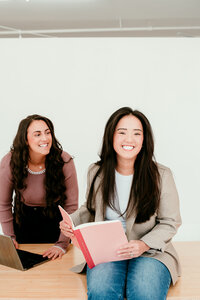 Two women entrepreneurs sitting with laptops and notebooks, laughing during a professional branding and headshot photography session in Minneapolis.