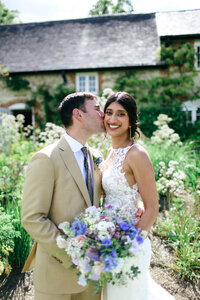 bride-smiling-as-groom-kisses-her-at-luxury-wedding-at-bury-court-barn-in-surrey-by-leslie-choucard-photography