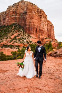 bride and groom holding hands smiling walking to camera with red rock background Sedona Arizona